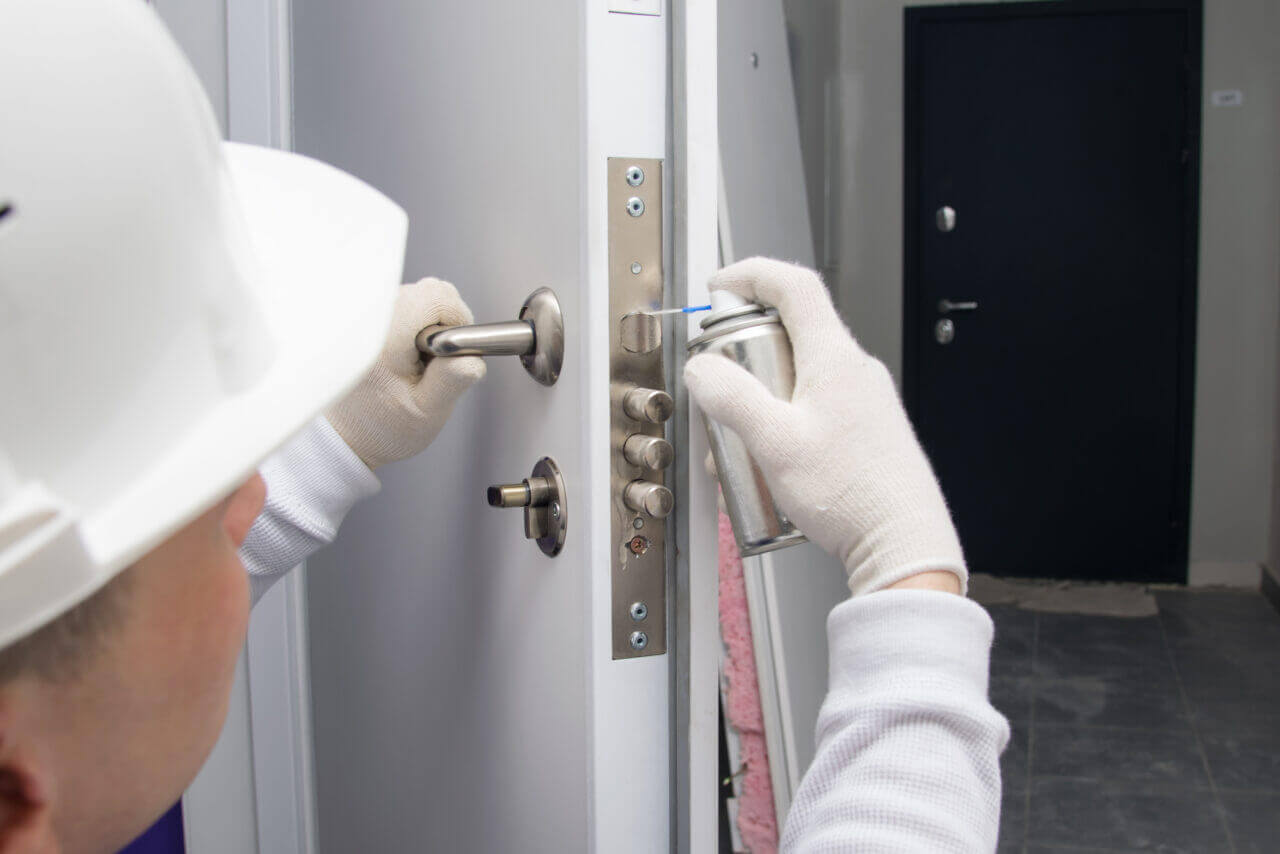 A locksmith lubricating a door lock