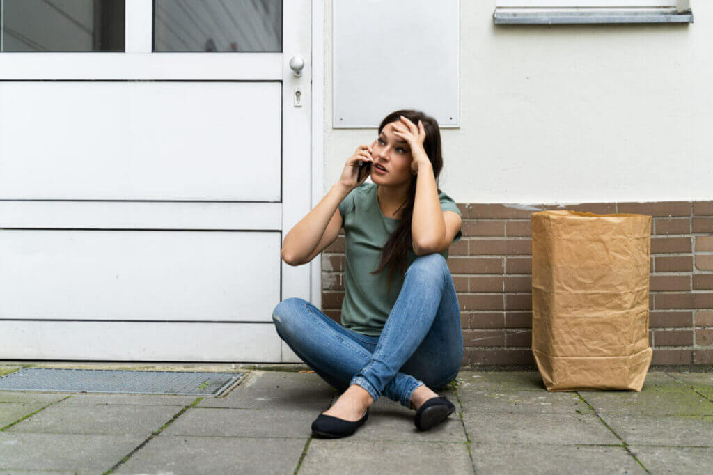 A stressed person sitting next to their home front door and calling a locksmith for house