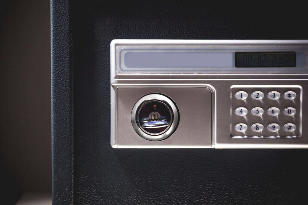 Close-up image of an electronic safe with a keypad and a circular combination dial, likely the work of a skilled locksmith. The keypad features numbers 0-9, and the display screen above it is blank. The safe boasts a sleek black exterior and a silver front panel.
