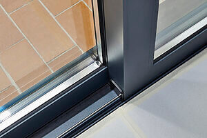 A close-up view of a sliding glass door with a metal frame, meticulously installed by a professional locksmith. The door leads out to an exterior area with a brick floor. The frame appears to be gray, and part of the floor inside is covered with white protective material.