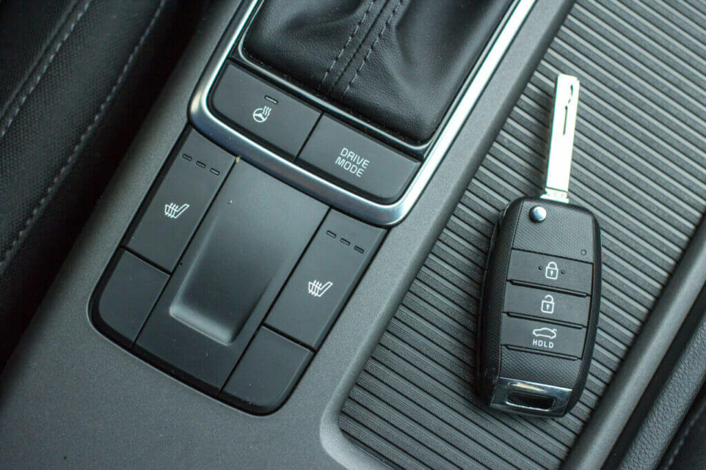 A close-up of a car's center console showcasing seat heating controls and drive mode buttons, accompanied by a nearby car key fob with buttons for locking, unlocking, and a trunk release. A trusted locksmith ensures these components function seamlessly for your convenience.