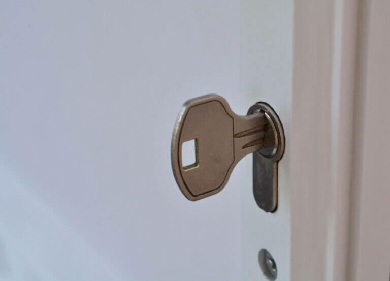 Close-up of a metal key, carefully inserted by a skilled locksmith, into a keyhole in a white door.