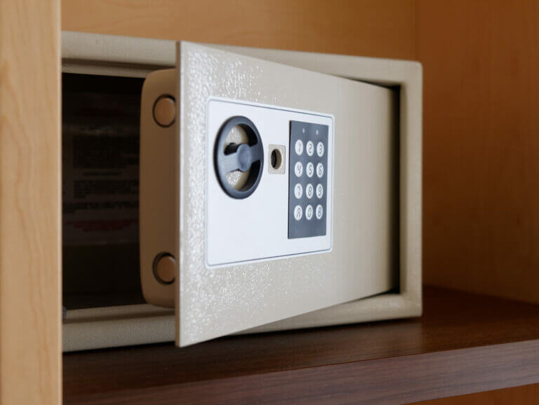 A small, beige electronic safe with a keypad and rotary handle is shown open on a wooden shelf. The safe, which looks like it was inspected by a locksmith, has a digital display and number pad for entering a security code.