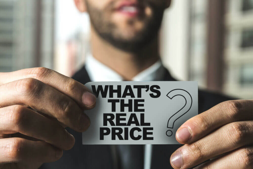 A man in a suit holds a card in front of him that reads, "WHAT'S THE REAL PRICE?" with a large question mark next to the text. The background shows out-of-focus buildings, hinting at the multifaceted world of city locksmith services.
